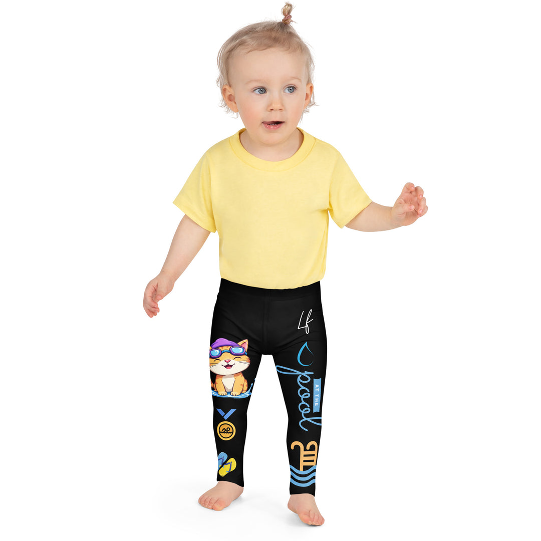 Aqua Kitty Winner Girls Leggings, black background with a blue and yellow swimmer cat wearing a diving mask and swim cap on one leg, golden medal and pool slippers below, "at the pool" text with water drop, and pool water with ladder on the other leg, front close-up view on model