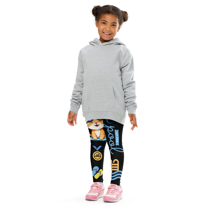 Aqua Kitty Winner Girls Leggings, black background with a blue and yellow swimmer cat wearing a diving mask and swim cap on one leg, golden medal and pool slippers below, "at the pool" text with water drop, and pool water with ladder on the other leg, front pose with arms at sides on model