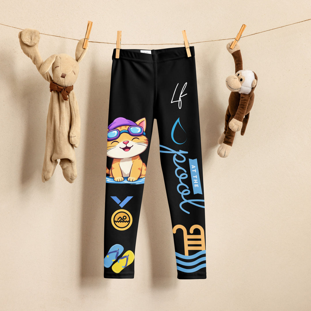Aqua Kitty Winner Girls Leggings, black background with a blue and yellow swimmer cat wearing a diving mask and swim cap on one leg, golden medal and pool slippers below, "at the pool" text with water drop, and pool water with ladder on the other leg, front view on hanger