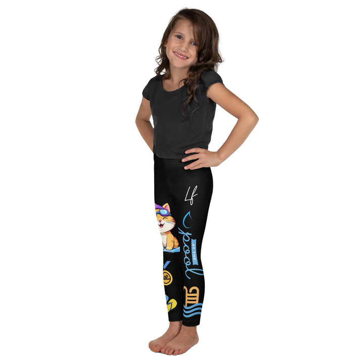 Aqua Kitty Winner Girls Leggings, black background with a blue and yellow swimmer cat wearing a diving mask and swim cap on one leg, golden medal and pool slippers below, "at the pool" text with water drop, and pool water with ladder on the other leg, left side view on model