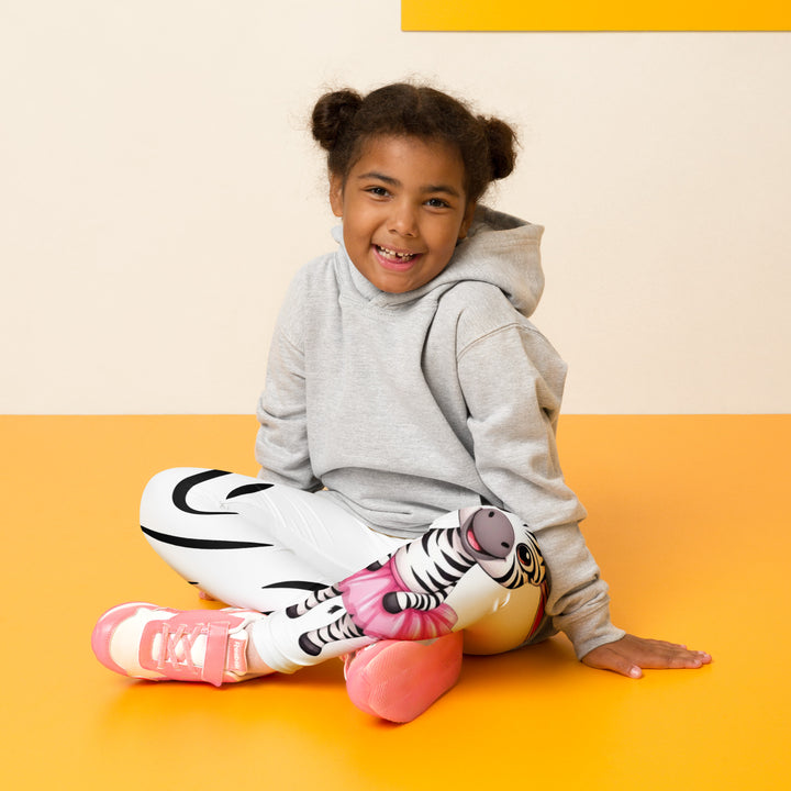  Ballet Black and White Zebra Girls Leggings, white background with a black and white zebra wearing a pink ballet skirt on the lower part of one leg, and black zebra stripes on the lower part of the other leg, seated pose on model