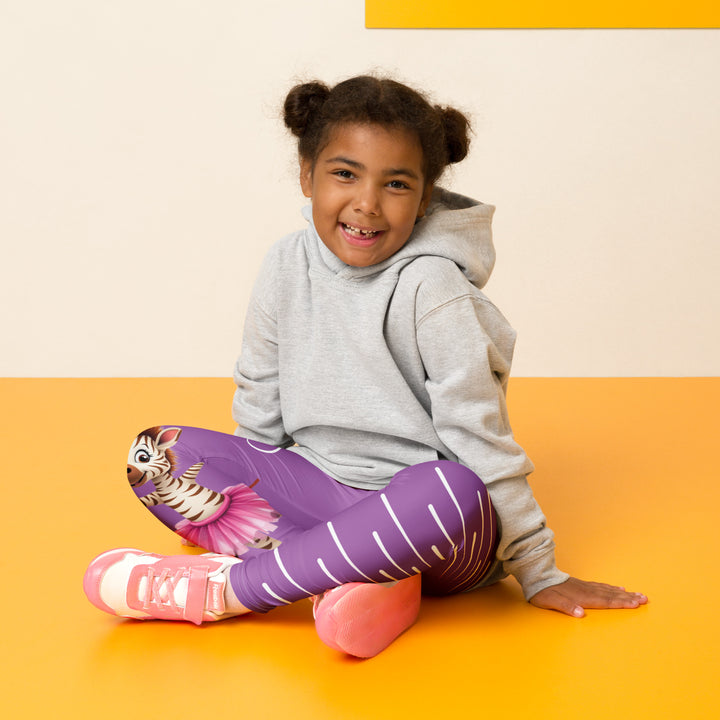 Ballet Sweet Zebra Girls Leggings, purple background with a brown and white zebra in a pink ballet skirt standing on one leg with arms extended, brown music notes above, and white vertical stripes running down the opposite leg, seated pose on model