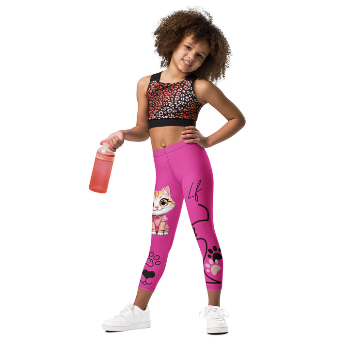 Cat Trace Girls Leggings, pink background with a yellow cat wearing a pink dress at the top of one leg, black paw prints and a black cat nose below, and a black line-drawn cat with black and cream paw prints on the other leg, relaxed front pose on model