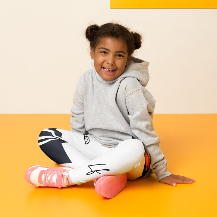  Chilly Penguin Girls Leggings, white background with a black and white small penguin sitting with green eyes on one leg, and a black and white iceberg with a wooden snow sign that says "NORTH POLE" on the other leg, seated pose on model