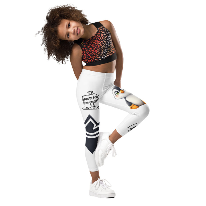 Chilly Penguin Girls Leggings, white background with a black and white small penguin sitting with green eyes on one leg, and a black and white iceberg with a wooden snow sign that says "NORTH POLE" on the other leg, side view with one leg lifted and bent on model
