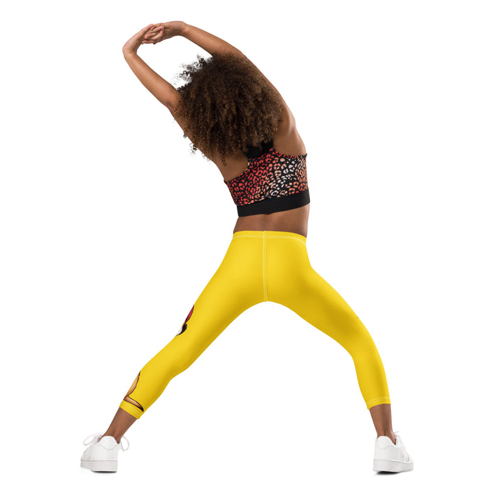 Cool Meerkat Girls Leggings, yellow background with a meerkat wearing a red cap on one leg and a paw graphic on the other leg appearing to come through the fabric, back angle with relaxed pose on model