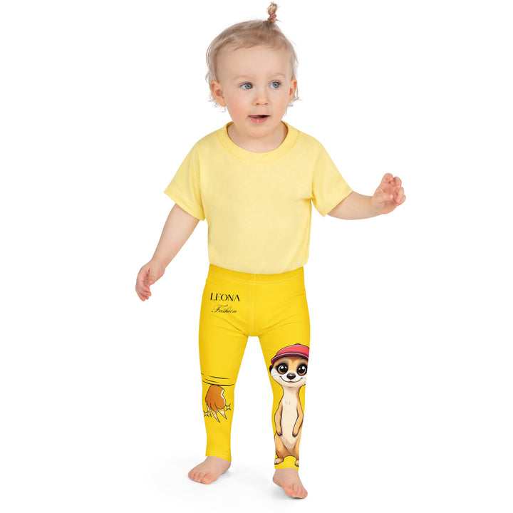 Cool Meerkat Girls Leggings, yellow background with a meerkat wearing a red cap on one leg and a paw graphic on the other leg appearing to come through the fabric, front close-up view on model-with a visible 'Leona Fashion' text on the design