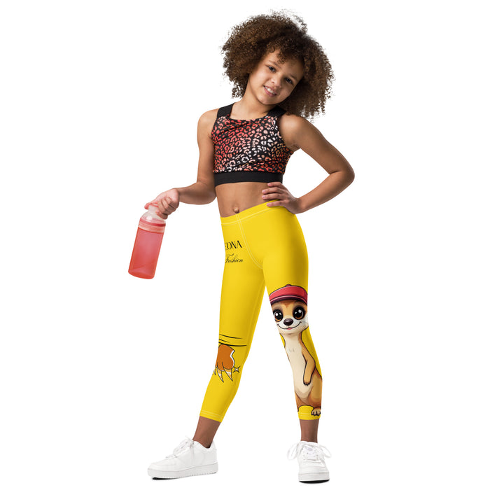 Cool Meerkat Girls Leggings, yellow background with a meerkat wearing a red cap on one leg and a paw graphic on the other leg appearing to come through the fabric, front view on model-with a visible 'Leona Fashion' text on the design