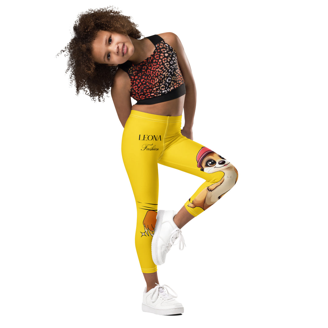  Cool Meerkat Girls Leggings, yellow background with a meerkat wearing a red cap on one leg and a paw graphic on the other leg appearing to come through the fabric, front view with one leg lifted and bent on model-with a visible 'Leona Fashion' text on the design