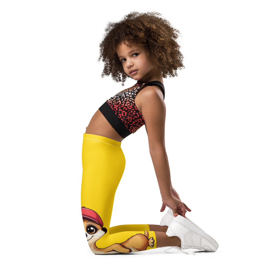 Cool Meerkat Girls Leggings, yellow background with a meerkat wearing a red cap on one leg and a paw graphic on the other leg appearing to come through the fabric, left side view kneeling on model
