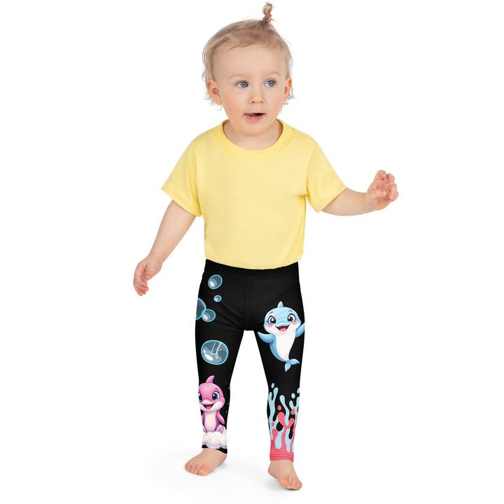 Coral Dolphin Girls Leggings, black background with a pink baby dolphin lying on a white cloud at the bottom of one leg and blue sea bubbles above, and a blue baby dolphin on the upper part of the other leg with pink and blue coral details at the bottom, front close-up view on model