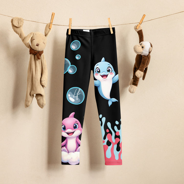 Coral Dolphin Girls Leggings, black background with a pink baby dolphin lying on a white cloud at the bottom of one leg and blue sea bubbles above, and a blue baby dolphin on the upper part of the other leg with pink and blue coral details at the bottom, front view on hanger