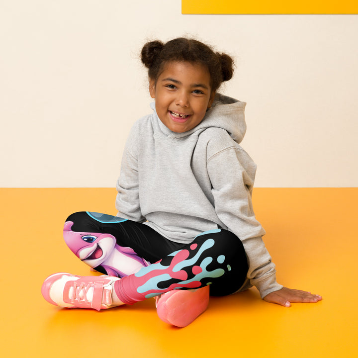 Coral Dolphin Girls Leggings, black background with a pink baby dolphin lying on a white cloud at the bottom of one leg and blue sea bubbles above, and a blue baby dolphin on the upper part of the other leg with pink and blue coral details at the bottom, seated pose on model