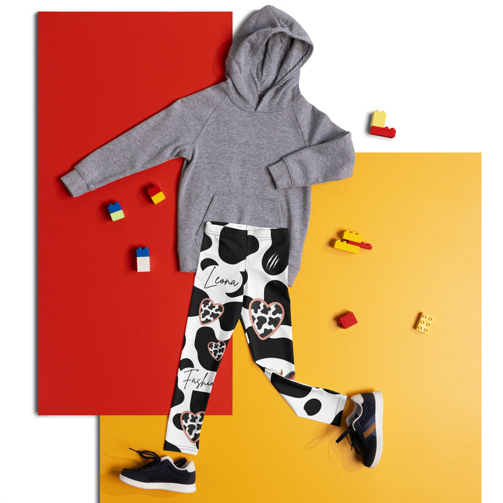  Cowlicious Love Girls Leggings, white background with black cow-like spots and a small black and white cow with a flower in its hair on one leg, front view laid flat on floor-with a visible 'Leona Fashion' text on the design