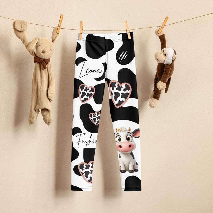 Cowlicious Love Girls Leggings, white background with black cow-like spots and a small black and white cow with a flower in its hair on one leg, front view on hanger-with a visible 'Leona Fashion' text on the design