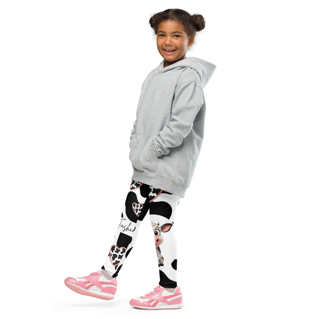 Cowlicious Love Girls Leggings, white background with black cow-like spots and a small black and white cow with a flower in its hair on one leg, front view with one leg lifted and extended on model-with a visible 'Leona Fashion' text on the design