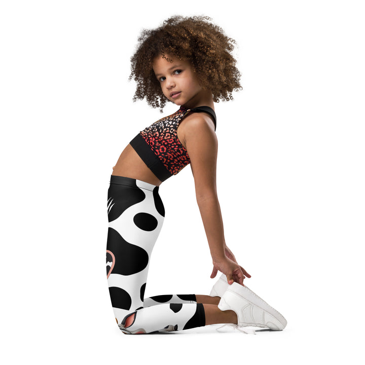  Cowlicious Love Girls Leggings, white background with black cow-like spots and a small black and white cow with a flower in its hair on one leg, left side view kneeling on model