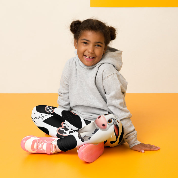 Cowlicious Love Girls Leggings, white background with black cow-like spots and a small black and white cow with a flower in its hair on one leg, seated pose on model