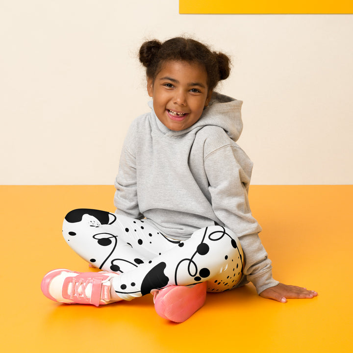 Dot & Line Girls Leggings, white background with black spots, lines, and dots interwoven throughout the design, seated pose on model