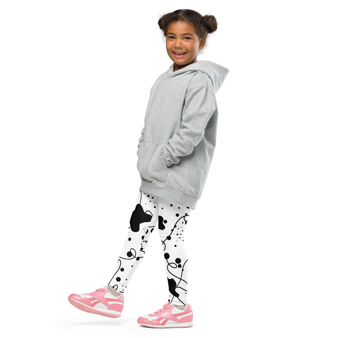 Dot & Line Girls Leggings, white background with black spots, lines, and dots interwoven throughout the design, side view with one leg lifted and extended on model
