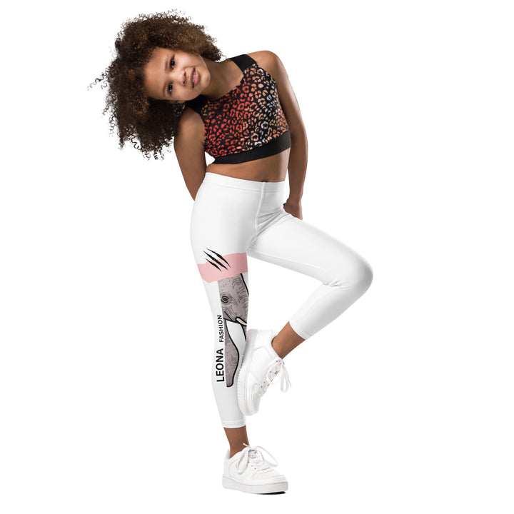 Elephant Whispers Girls Leggings, white background with gray elephant in profile on one leg, visible trunk, and soft blush pink stripe detail across the head, front view with one leg lifted and bent on model-with a visible 'Leona Fashion' text on the design