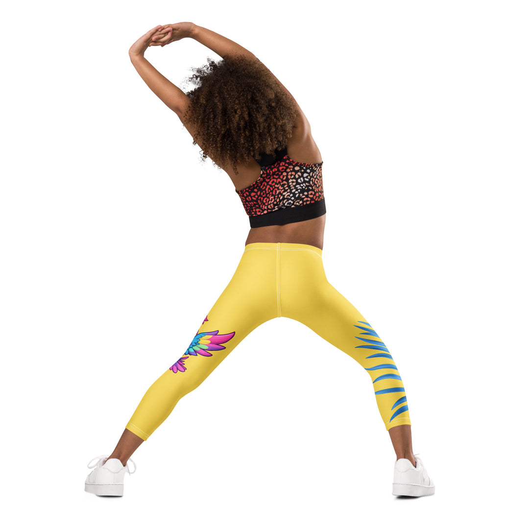Fly Baby Parrot Girls Leggings, yellow background with a small pink baby parrot with spread wings on one leg, and a large blue tropical leaf with "I CAN DO IT" text in blue and pink letters above it on the other leg, back angle with relaxed pose on model