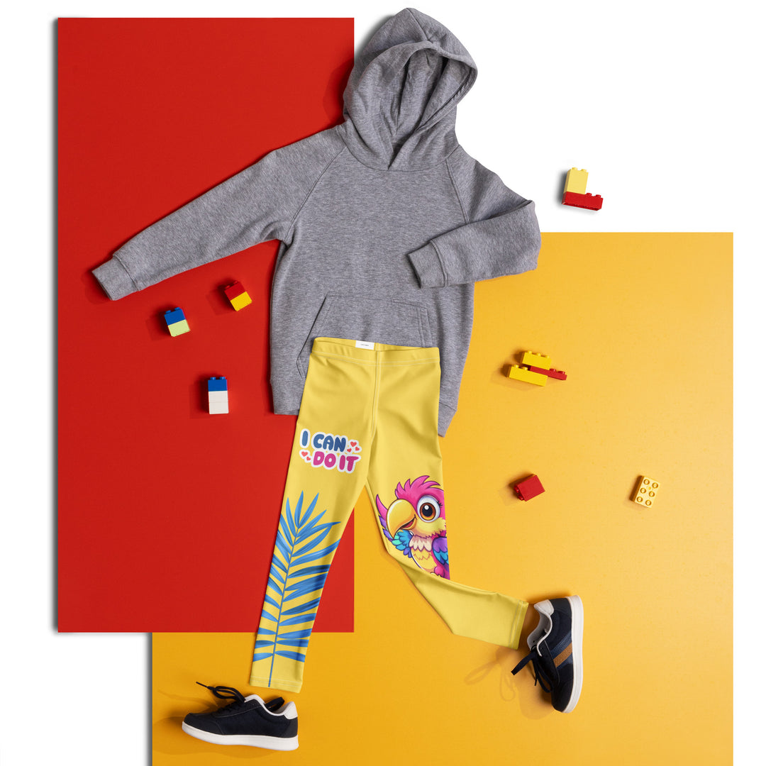 Fly Baby Parrot Girls Leggings, yellow background with a small pink baby parrot with spread wings on one leg, and a large blue tropical leaf with "I CAN DO IT" text in blue and pink letters above it on the other leg, front view laid flat on floor