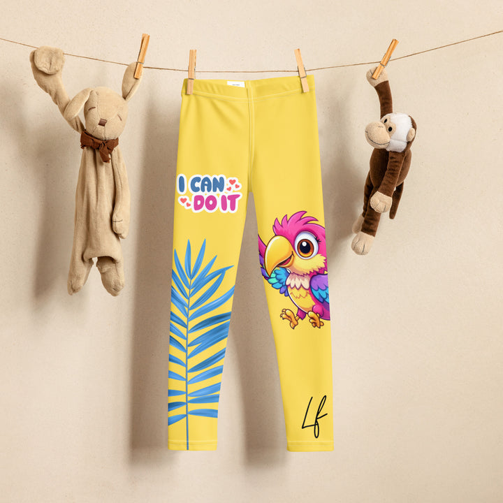 Fly Baby Parrot Girls Leggings, yellow background with a small pink baby parrot with spread wings on one leg, and a large blue tropical leaf with "I CAN DO IT" text in blue and pink letters above it on the other leg, front view on hanger