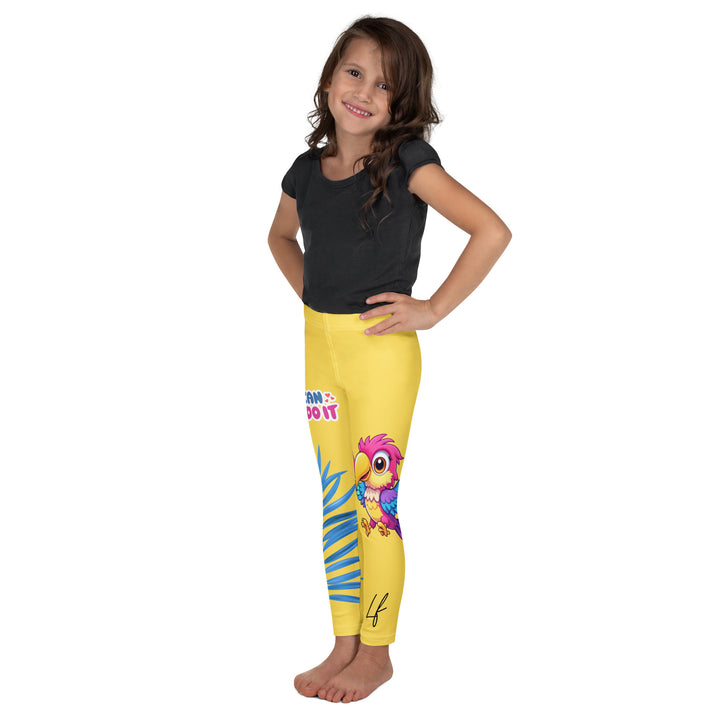 Fly Baby Parrot Girls Leggings, yellow background with a small pink baby parrot with spread wings on one leg, and a large blue tropical leaf with "I CAN DO IT" text in blue and pink letters above it on the other leg, left side view on model