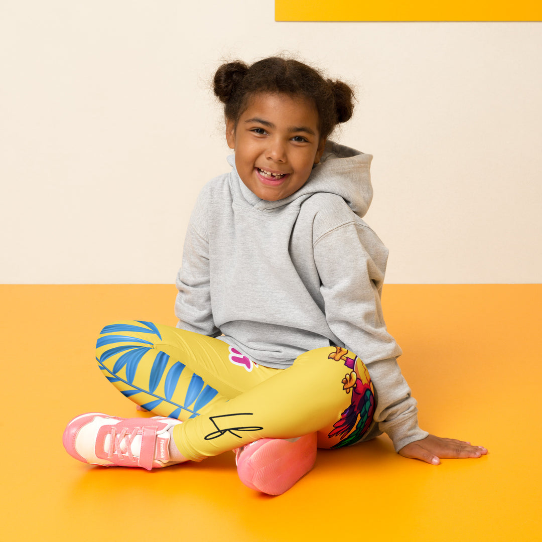  Fly Baby Parrot Girls Leggings, yellow background with a small pink baby parrot with spread wings on one leg, and a large blue tropical leaf with "I CAN DO IT" text in blue and pink letters above it on the other leg, seated pose on model