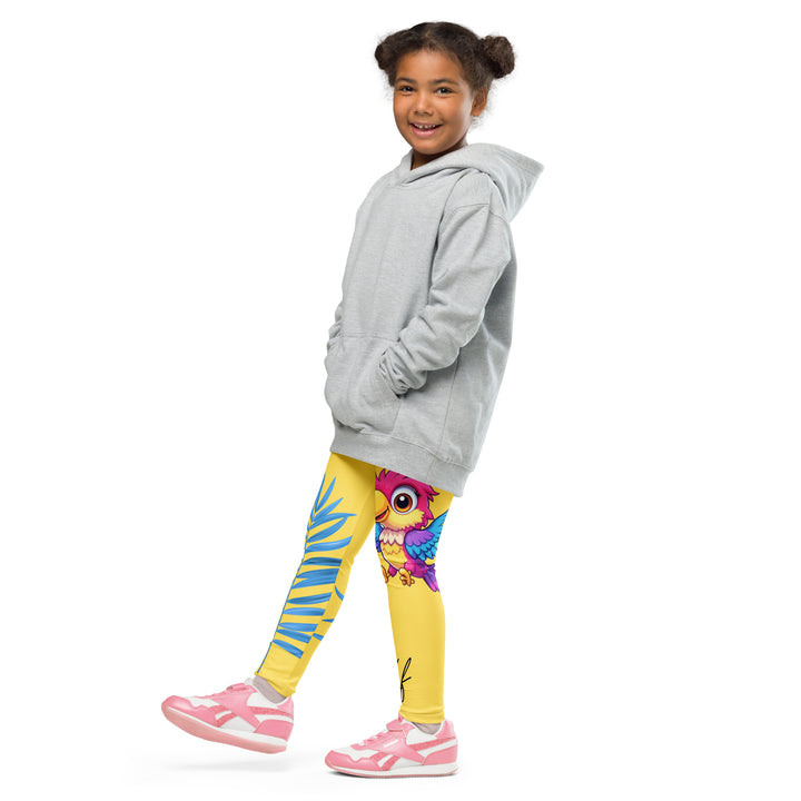  Fly Baby Parrot Girls Leggings, yellow background with a small pink baby parrot with spread wings on one leg, and a large blue tropical leaf with "I CAN DO IT" text in blue and pink letters above it on the other leg, side view with one leg lifted and extended on model