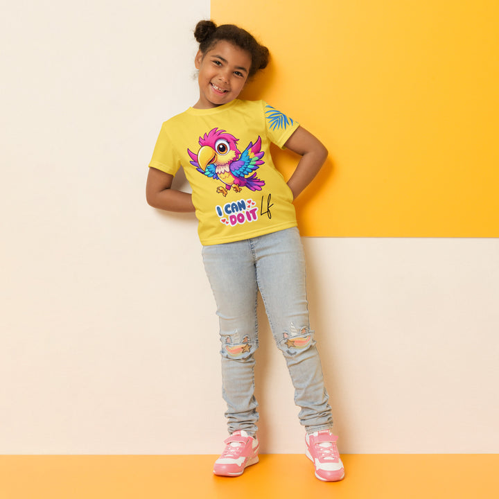 Fly Baby Parrot Girls T-shirt, yellow background with a small pink baby parrot with spread wings on the front, "I CAN DO IT" text in blue and pink letters below, and a blue tropical leaf on the left sleeve, relaxed front pose on model
