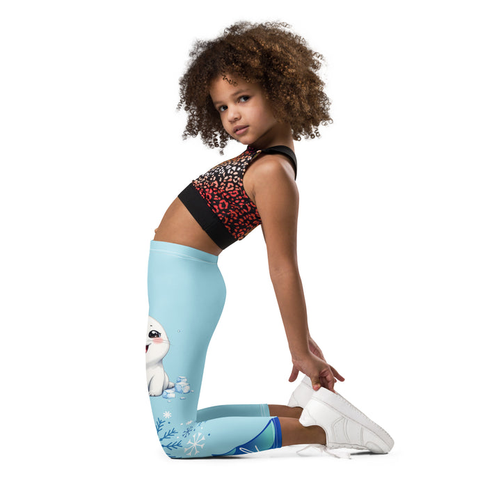 Frosty Seal Girls Leggings, light sky blue background with a white baby seal, blue and white snowflakes, and an ice block on one leg, and blue and white ice cubes with snowflakes on the other leg, left side view kneeling on model