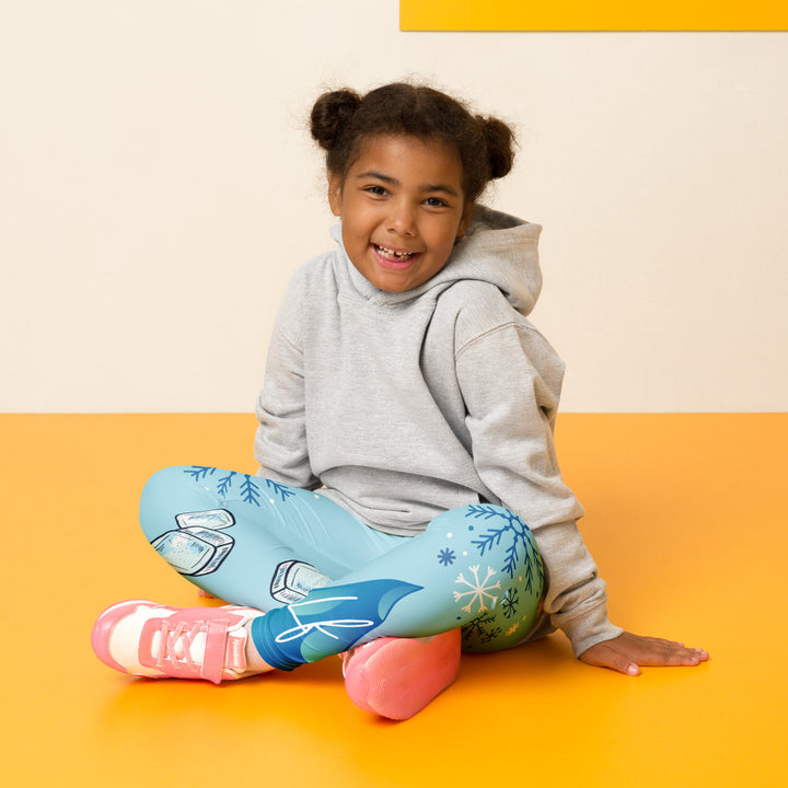 Frosty Seal Girls Leggings, light sky blue background with a white baby seal, blue and white snowflakes, and an ice block on one leg, and blue and white ice cubes with snowflakes on the other leg, seated pose on model