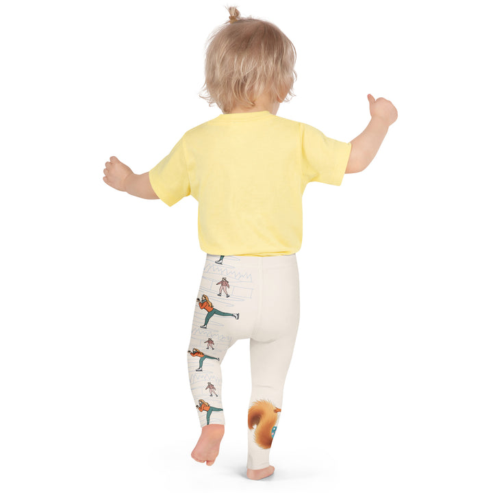 Frosty Twirl Squirrel Girls Leggings, beige background with a brown squirrel ice skating in a blue polka dot dress on one leg, ice trail lines, mountains, and small ice skaters along the other leg, in blue, brown, and orange tones, back pose with one arm on hip on model