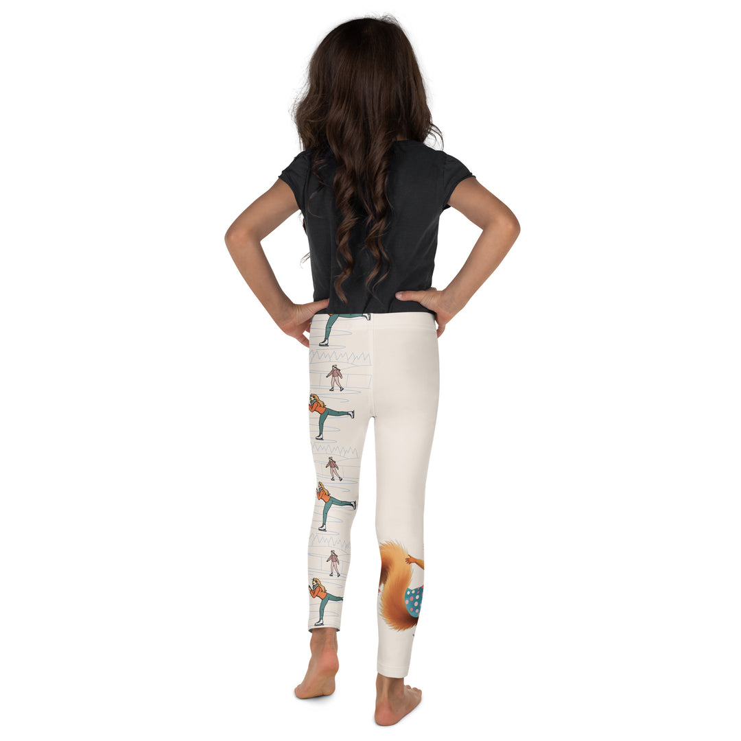 Frosty Twirl Squirrel Girls Leggings, beige background with a brown squirrel ice skating in a blue polka dot dress on one leg, ice trail lines, mountains, and small ice skaters along the other leg, in blue, brown, and orange tones, back view on model