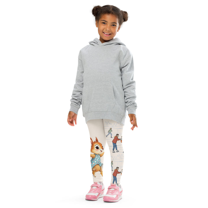 Frosty Twirl Squirrel Girls Leggings, beige background with a brown squirrel ice skating in a blue polka dot dress on one leg, ice trail lines, mountains, and small ice skaters along the other leg, in blue, brown, and orange tones, front pose with arms at sides on model