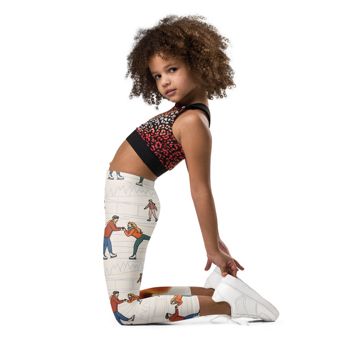  Frosty Twirl Squirrel Girls Leggings, beige background with a brown squirrel ice skating in a blue polka dot dress on one leg, ice trail lines, mountains, and small ice skaters along the other leg, in blue, brown, and orange tones, left side view kneeling on model
