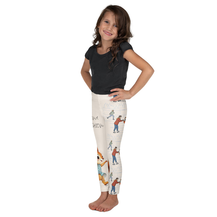 Frosty Twirl Squirrel Girls Leggings, beige background with a brown squirrel ice skating in a blue polka dot dress on one leg, ice trail lines, mountains, and small ice skaters along the other leg, in blue, brown, and orange tones, right side view on model