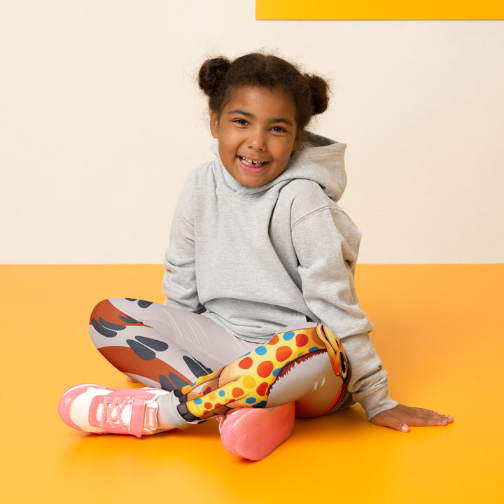  Giraffe Path Girls Leggings, cream background with a yellow giraffe featuring colorful polka dots on one leg, and orange-brown spots with dark gray giraffe footprints on the other leg, both designs starting from above the knee down, seated pose on model