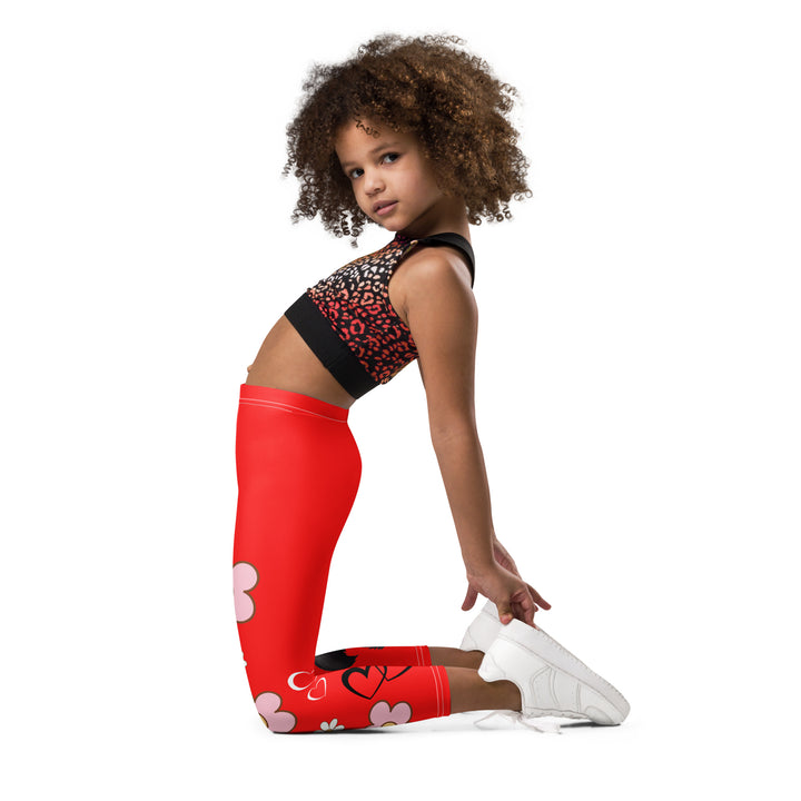Heart Stinker Girls Leggings, red background with a black and white skunk holding a white flower in its hand, featuring white hearts and pink-and-white floral elements, left side view kneeling on model