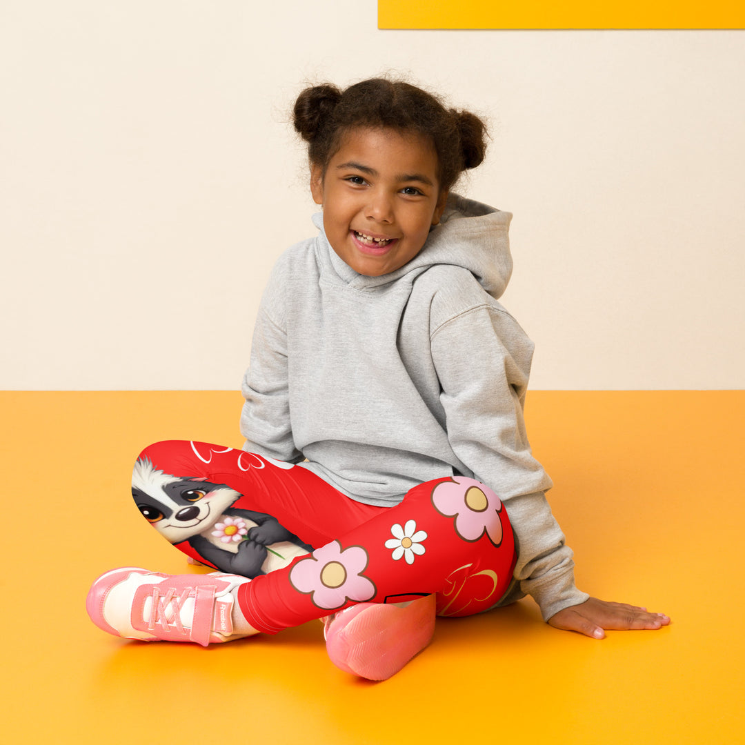 Heart Stinker Girls Leggings, red background with a black and white skunk holding a white flower in its hand, featuring white hearts and pink-and-white floral elements, seated pose on model