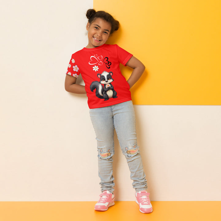Heart Stinker Girls T-shirt, red background with a black and white skunk holding a white flower in its hand, black and white hearts and a white flower above, and pink-and-white floral details on the right sleeve, relaxed front pose on model