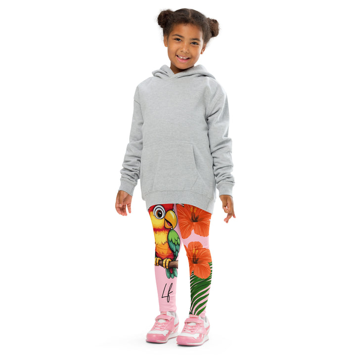 Jungle Parrot Girls Leggings, light pink background with a red, yellow, orange, and green parrot standing on a branch on one leg, and green jungle leaves with two large orange flowers running down the other leg, front pose with arms at sides on model