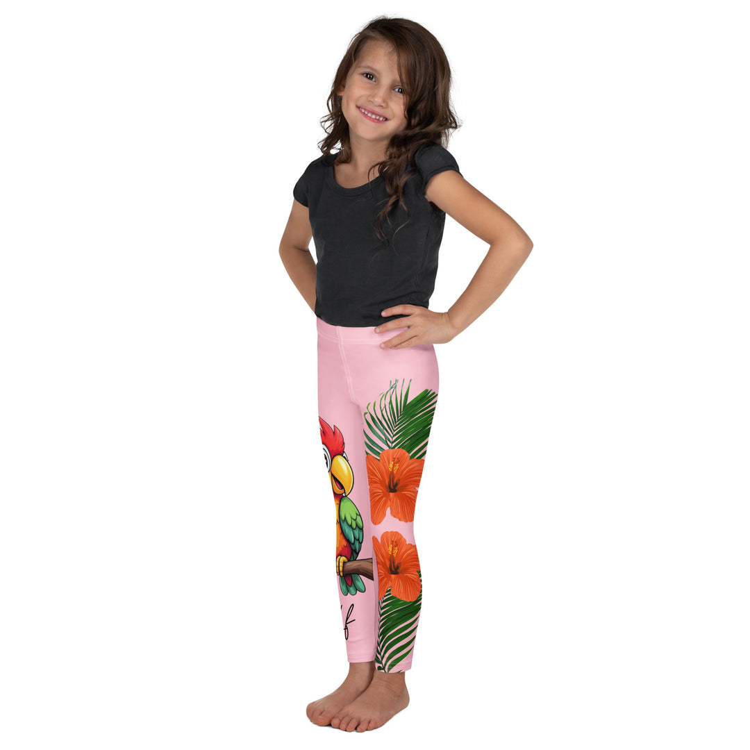Jungle Parrot Girls Leggings, light pink background with a red, yellow, orange, and green parrot standing on a branch on one leg, and green jungle leaves with two large orange flowers running down the other leg, left side view on model