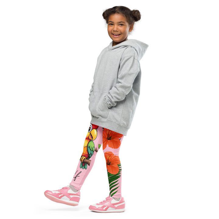 Jungle Parrot Girls Leggings, light pink background with a red, yellow, orange, and green parrot standing on a branch on one leg, and green jungle leaves with two large orange flowers running down the other leg, side view with one leg lifted and extended on model