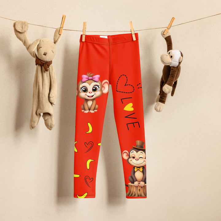 Love Monkey Girls Leggings, red background with a smiling female monkey with big eyes and a pink bow on the head at the top of one leg, yellow bananas with black drawn hearts below, and a winking male monkey wearing a hat sitting on a stump at the bottom of the other leg with "LOVE" text above, front view on hanger