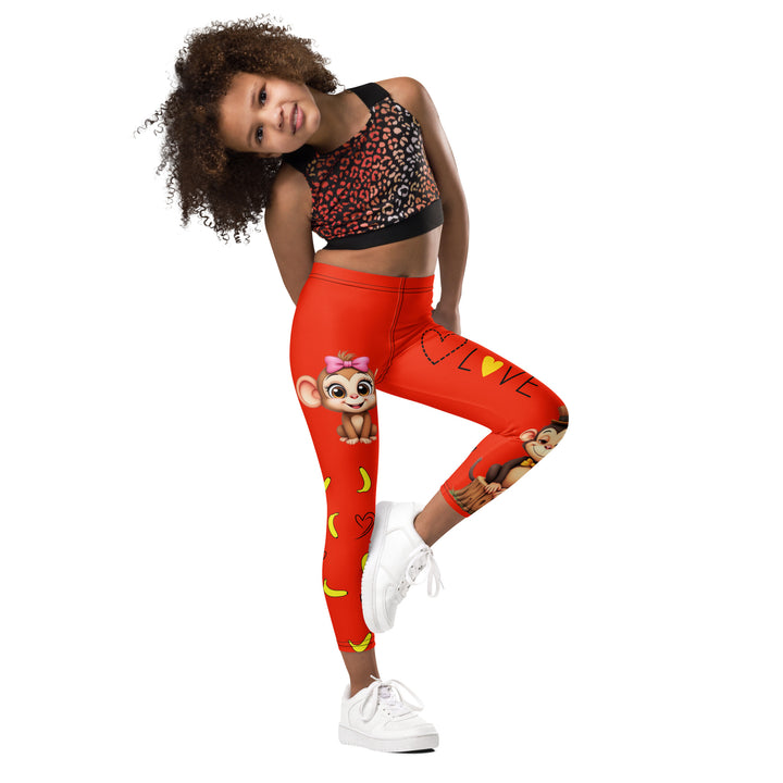  Love Monkey Girls Leggings, red background with a smiling female monkey with big eyes and a pink bow on the head at the top of one leg, yellow bananas with black drawn hearts below, and a winking male monkey wearing a hat sitting on a tree stump near the bottom of the other leg, with the word "LOVE" above, side view with one leg lifted and bent on model