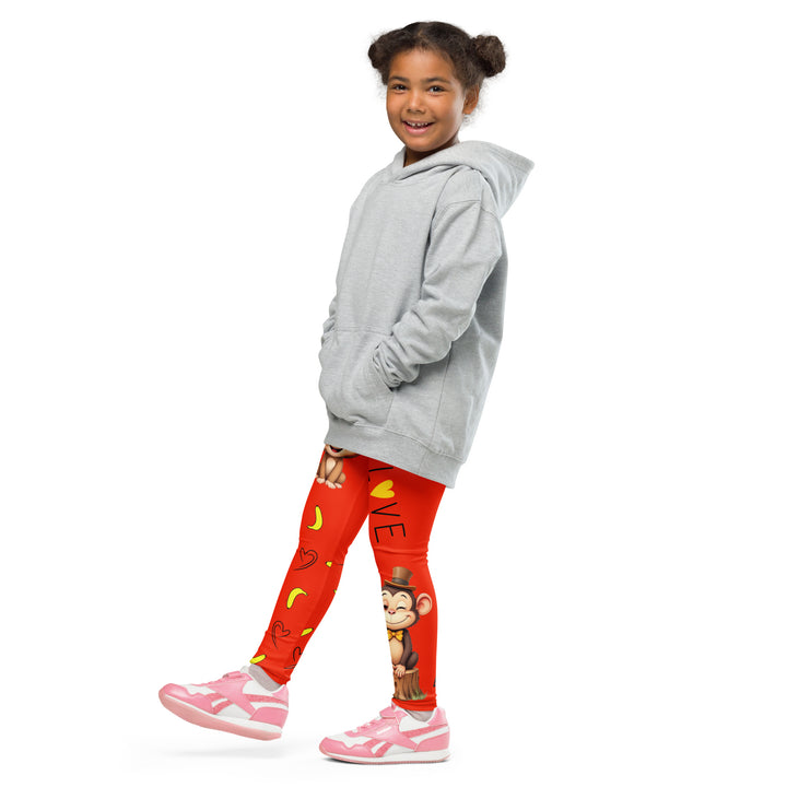 Love Monkey Girls Leggings, red background with a smiling female monkey with big eyes and a pink bow on the head at the top of one leg, yellow bananas with black drawn hearts below, and a winking male monkey wearing a hat sitting on a tree stump near the bottom of the other leg, with the word "LOVE" above, side view with one leg lifted and extended on model