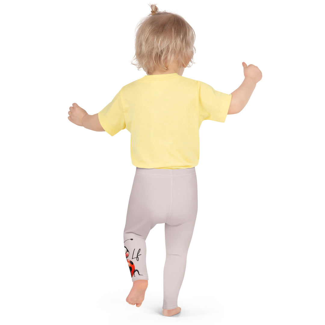 Lovebugs Girls Leggings, sand-colored background with a female ladybug with big eyes at the bottom of one leg and a male ladybug looking delighted on the other leg, with black swirling lines above them forming hearts on both sides, back pose on model